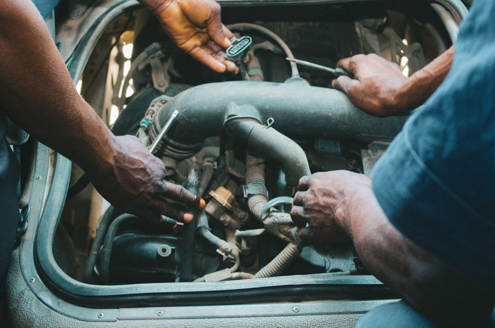 Mechanics' hands working together inside an engine bay